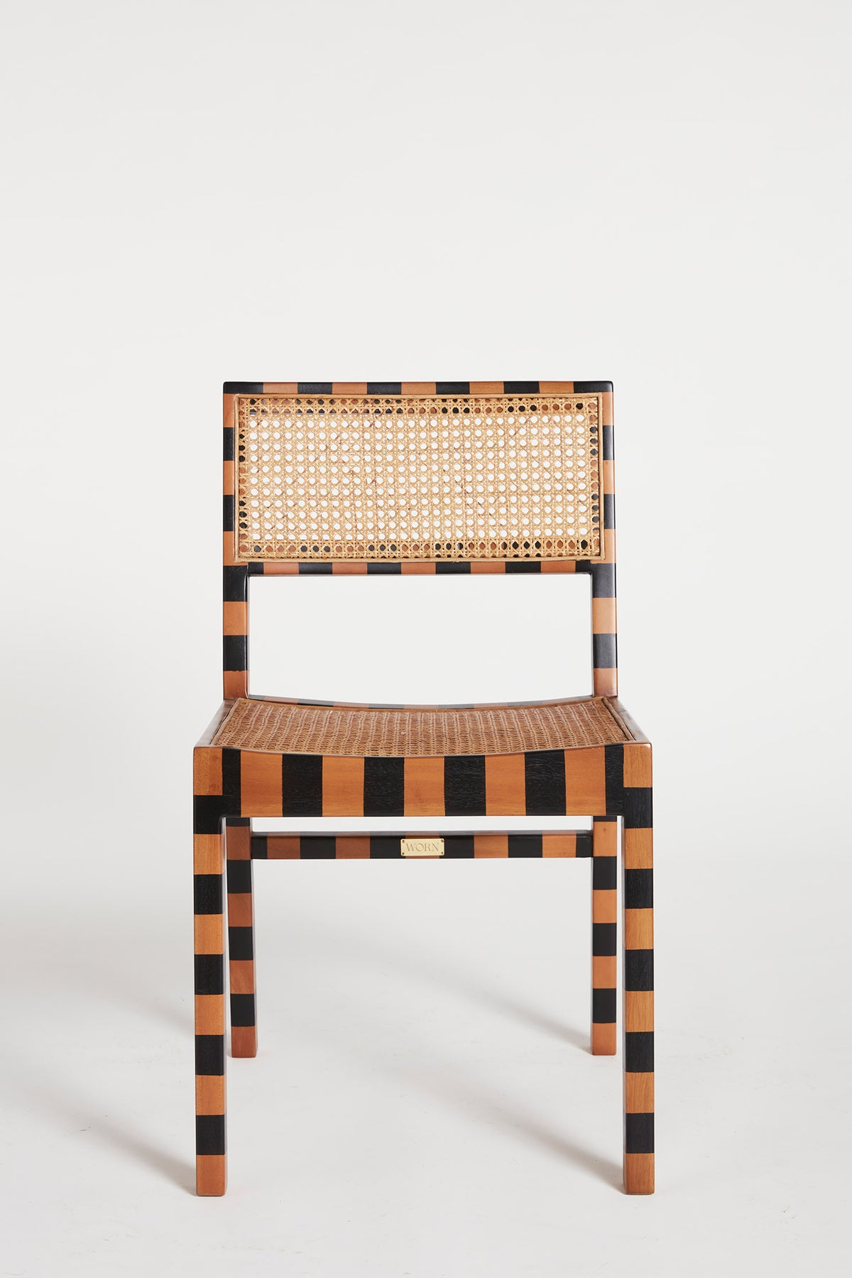 The Stripe Tisse Chair is a dining chair featuring timber frame painted with black and woven stripes. Seat and back both feature woven rattan panels.